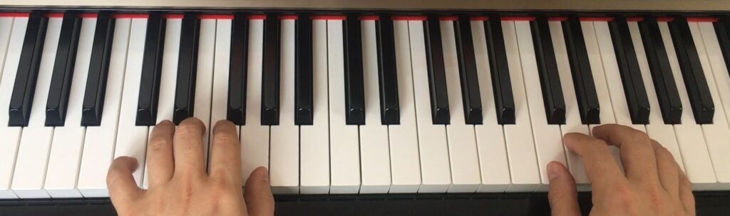 Les deux mains sur 1 clavier de piano : démarrez l'aventure aujourd'hui ! La main gauche joue dans les graves, et la main droite dans les aigües, 2 octaves au dessus. Les mains sont positionnées pour jouer un accord de Do majeur.